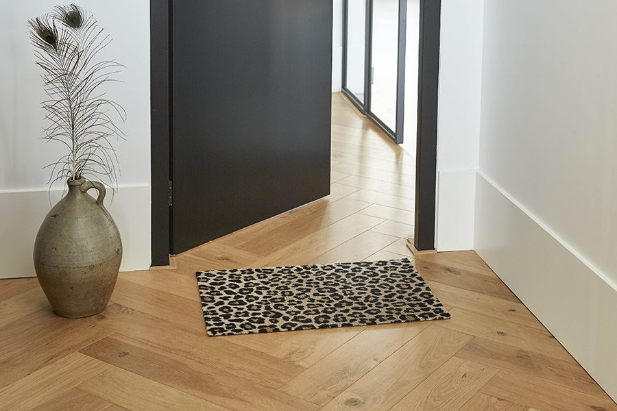 Eingangsbereich mit geöffneter Tür und Holzboden. Vor der Tür liegt eine flauschige Fußmatte mit Leopardenmuster. 