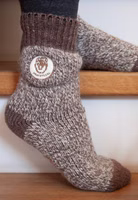jemand sitzend auf Treppenstufen mit einem Paar braun melierten Prachtkerl Stricksocken mit Löwenkopf-Patch und dunkelbraun abgesetztem Bündchen und Fersen-Zehen-Bereich