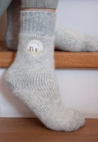 jemand sitzend auf Treppenstufen mit einem Paar hellgrau melierten Unschuldslamm Stricksocken mit Schäfchen-Patch und etwas dunkler grau abgesetztem Bündchen sowie Fersen- und Zehenbereich