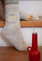 jemand sitzend auf Treppenstufen mit einem Paar hellbeige melierten Glücklich Stricksocken mit goldener Kleeblattstickerei im oberen Bereich