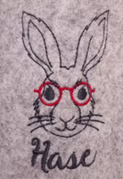 Nahaufnahme der Alter Hase Stickerei mit Hasenkopf und dunkelgrau und roter Brille auf grauem Filz