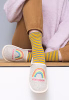 ein Paar hellbeige Filzpantoffeln mit Regenbogen-Stickerei, darunter der Schriftzug Kunterbunt in pink und außen cremefarbende Einfassung