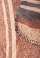 Nahaufnahme einer hellbraunen Kuscheldecke mit braunem Wappen und röhrendem Hirsch sowie dem Schriftzug Platzhirsch oben drüber. Oben und unten dunkelbraune und graue Streifen als Abschluss der kurzen Seiten
