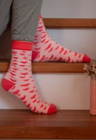sitzend auf Treppenstufen mit einem Paar rosa Zuckersüss Socken mit Herz-Allover in korallrot sowie abgesetzte Bündchen, Fersen- und Zehenbereiche in korallrot