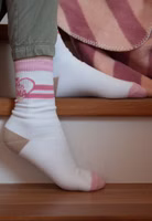 jemand sitzend auf Treppenstufen mit einem Paar weißen Sport-Socken mit rosa abgesetztem Bündchen sowie Zehenbereich und hellbraun abgesetztem Fersenbereich. Dazu im oberen Knöchelbereich rosa Streifen sowie ein Herz mit Beste Mama der Welt Schriftzug