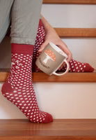 jemand sitzend auf Treppenstufen mit einem Paar dunkelrote Glückspilz Socken mit weißen Punkten, uni rot abgesetztem Bündchen-, Fersen- und Zehenbereich sowie oberhalb des Knöchels dem Motiv eines Fliegenpilzes und dem Schriftzug Glückspilz