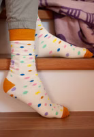 jemand sitzend auf Treppenstufen mit einem Paar cremefarbene Kunterbunt Socken mit bunten Punkten, uni senffarben abgesetztem Bündchen-, Fersen- und Zehenbereich sowie oberhalb des Knöchels dem bunten Schriftzug Kunterbunt