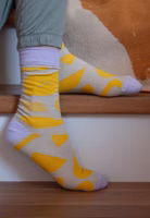 jemand sitzend auf Treppenstufen mit einem Paar beige Easy-Peasy-Socken mit gelben Motivelementen wie der Zitrone von Anna-Katharina Jansen und lila abgesetztem Bündchen-, Fersen- und Zehenbereich