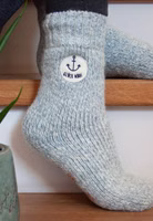 jemand sitzend auf Treppenstufen mit einem Paar hellblau melierte Glück ahoi Stricksocken mit dem Motivpatch eines Ankers