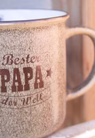 auf einer Holzleiter stehend ein hellbrauner Henkelbecher aus Porzellan mit dunkelbraunem Schriftzug "Bester Papa der Welt" vorne. Becher innen weiß.