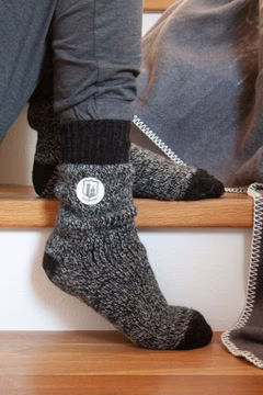 jemand sitzend auf Treppenstufen mit einem Paar schwarz melierten Hausherr Stricksocken mit Burg-Patch und schwarz abgesetztem Bündchen und Fersen-Zehen-Bereich