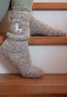 jemand sitzend auf Treppenstufen mit einem Paar hellbraun melierten Weltenbummlerin Stricksocken mit süßer Lama-Stickerei im oberen Bereich