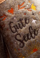 dunkelbrauner "Gute Seele" Schriftzug gestickt auf hellbraunem Filz, drumherum in warmen Gelb- und Orangetönen kleine Stickereien wie Sonne, Blumen, Herz