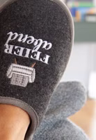 auf dem Sofa liegend ein schwarzer Filzpantoffel mit Feierabend-Schriftzug und Sessel-Stickerei