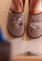 am Fuß hellbraune Filzpantoffeln mit der Stickerei von Handwerkuntensilien und dem Schriftzug Heimwerker in creme und dunkelbraun. Außen braun eingefasst und dunkelbraune Innensohle