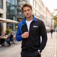 A man is walking down the street, wearing an OMKA tracksuit jacket with a stand-up collar. A subway sign is visible in the background.