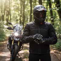 Motorradfahrer in schwarzer Textiljacke zieht Schutzhandschuhe an vor einer Reiseenduro auf einem sonnigen Waldweg